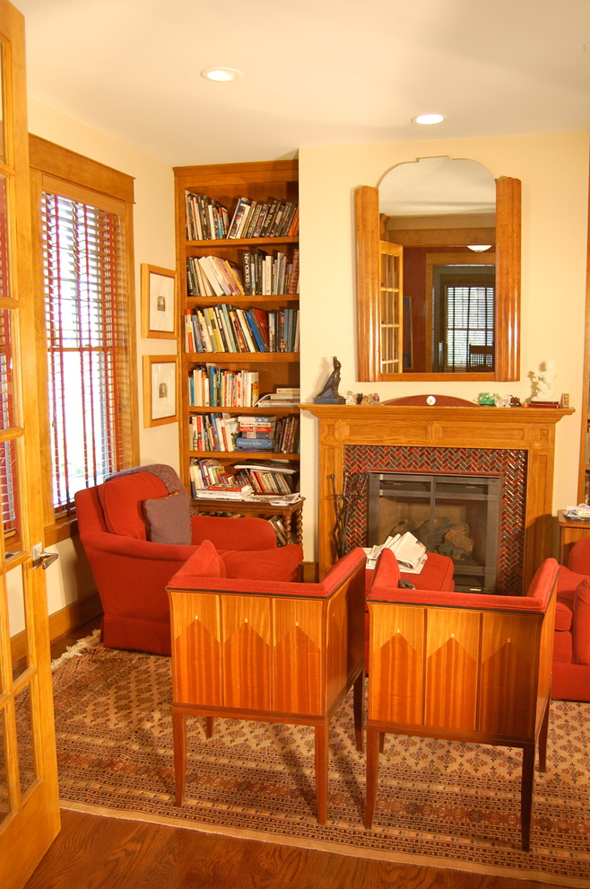 Inredning av ett amerikanskt hemmabibliotek, med ett fristående skrivbord, beige väggar, mellanmörkt trägolv, en standard öppen spis och en spiselkrans i trä