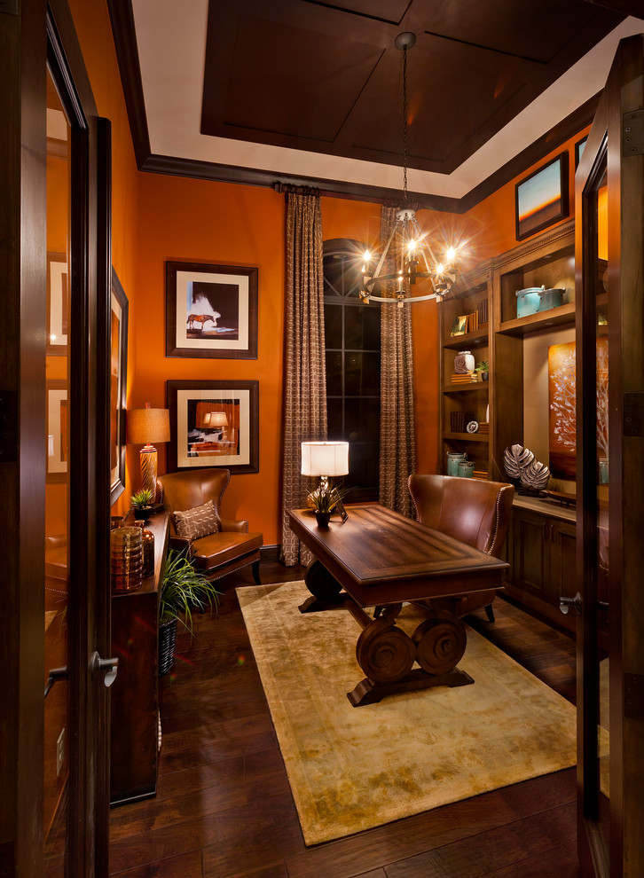 Exempel på ett stort klassiskt hemmabibliotek, med mörkt trägolv, ett fristående skrivbord och orange väggar