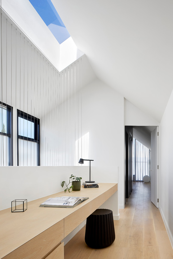 Idee per un piccolo studio minimal con pareti bianche, parquet chiaro, scrivania incassata e pavimento beige