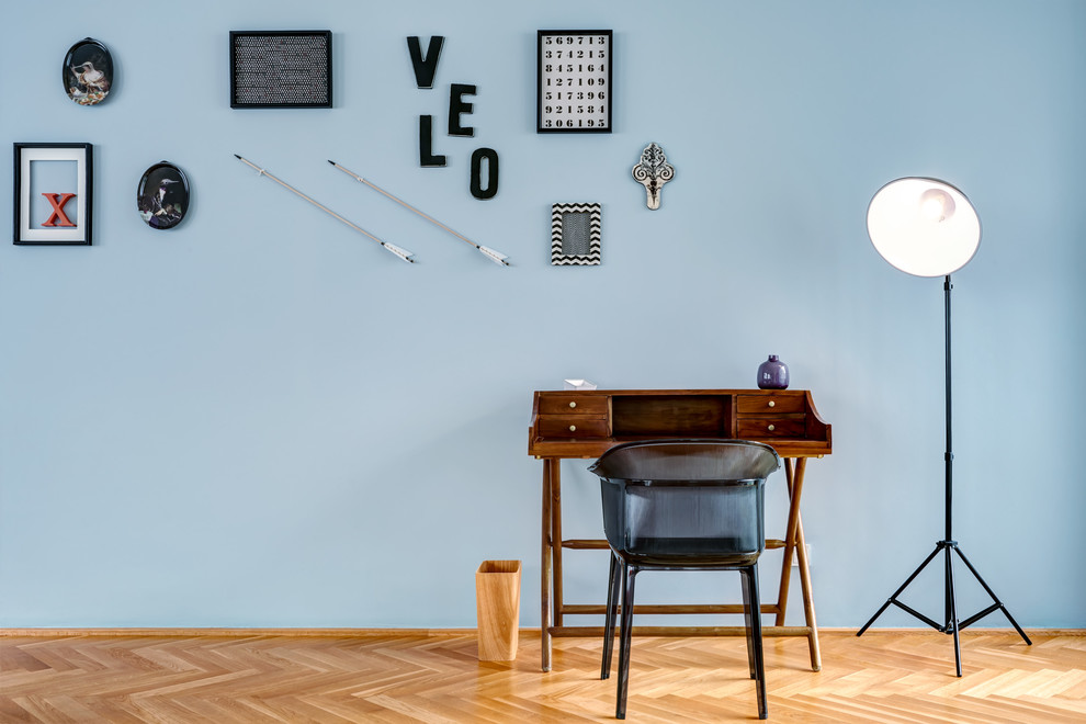 Mittelgroßes Modernes Arbeitszimmer ohne Kamin mit Arbeitsplatz, blauer Wandfarbe, braunem Holzboden, freistehendem Schreibtisch und beigem Boden in Berlin