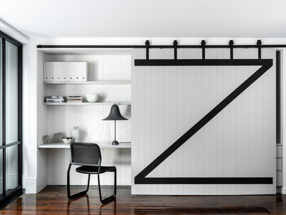 シドニーにあるインダストリアルスタイルのおしゃれな書斎 (白い壁、濃色無垢フローリング、造り付け机、茶色い床、パネル壁) の写真