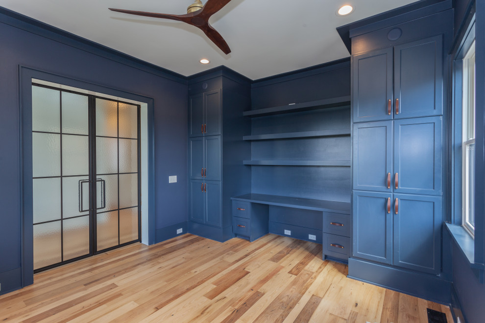 Cette photo montre un grand bureau bord de mer avec une bibliothèque ou un coin lecture, un mur bleu, parquet clair et un bureau intégré.