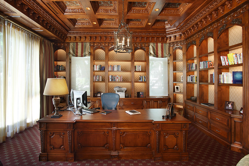 Inspiration för stora klassiska hemmabibliotek, med bruna väggar, heltäckningsmatta, ett fristående skrivbord och rött golv