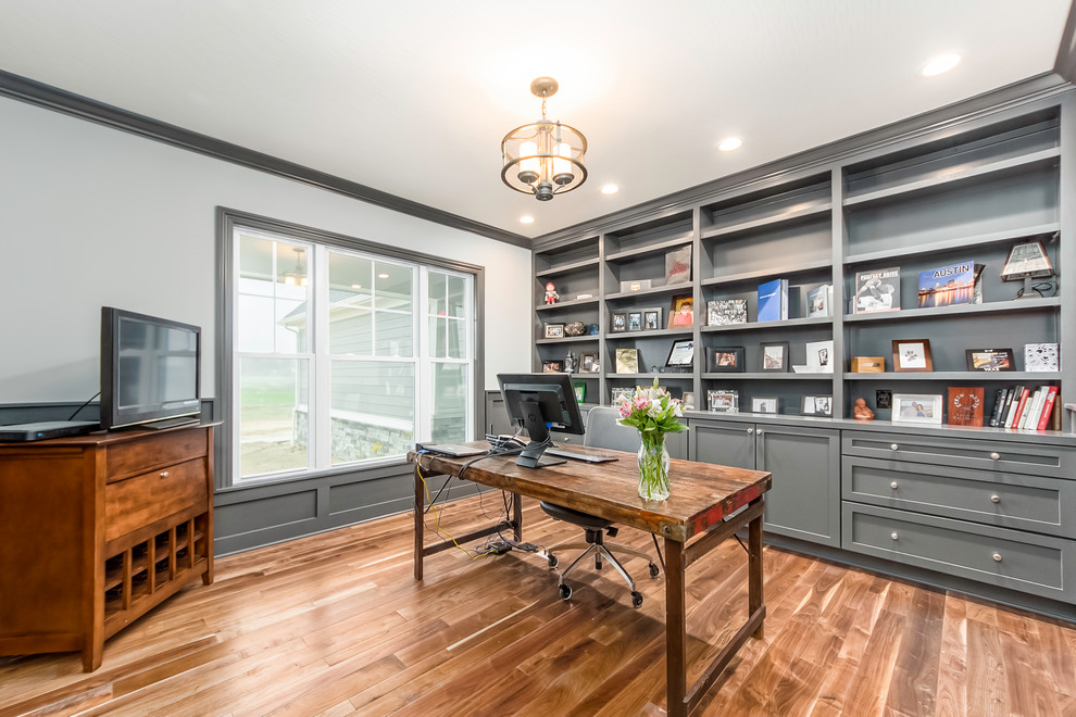 Modelo de despacho clásico renovado con paredes grises, suelo de madera en tonos medios, escritorio independiente y suelo marrón