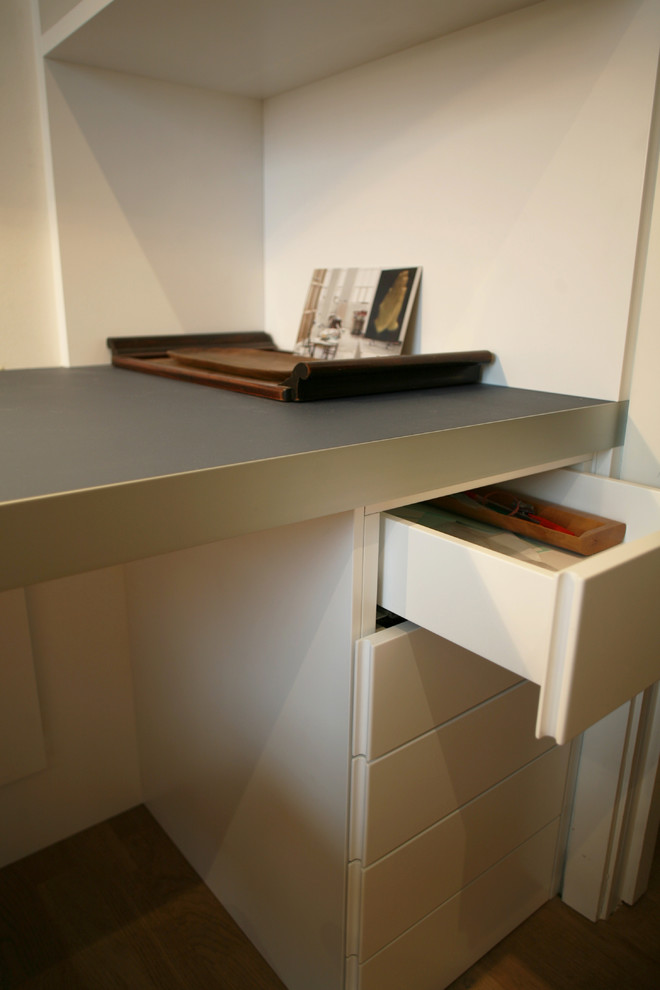 Ejemplo de despacho actual pequeño con paredes blancas, suelo de madera clara y escritorio empotrado