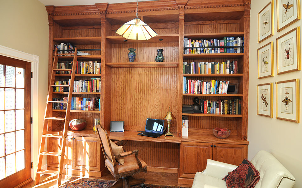 Klassisk inredning av ett mellanstort hemmabibliotek, med beige väggar, mörkt trägolv och ett inbyggt skrivbord