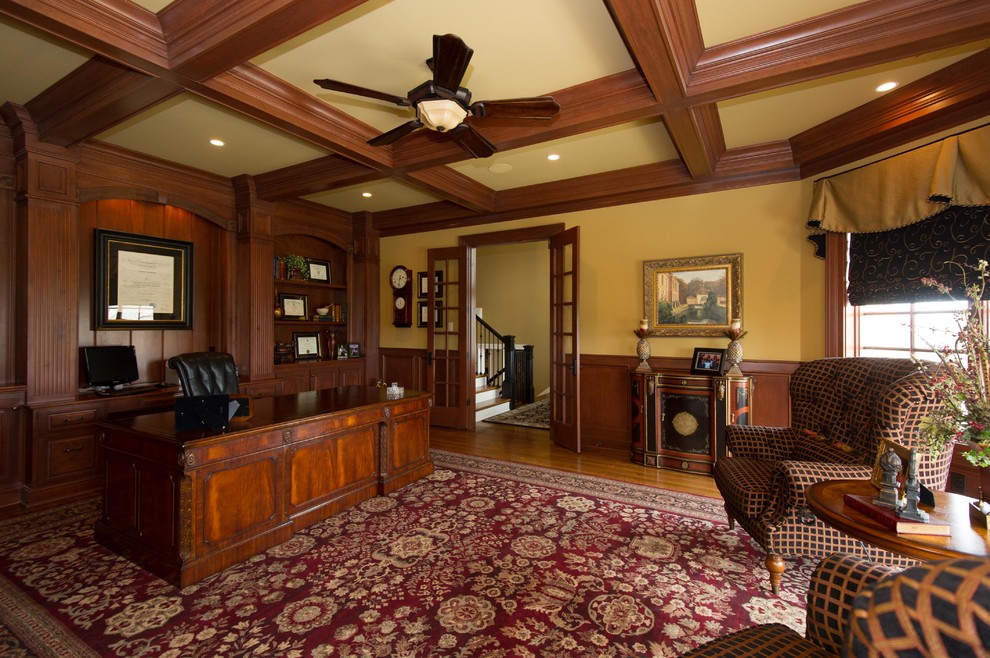 Foto de despacho clásico extra grande sin chimenea con suelo de madera en tonos medios, escritorio independiente y paredes amarillas
