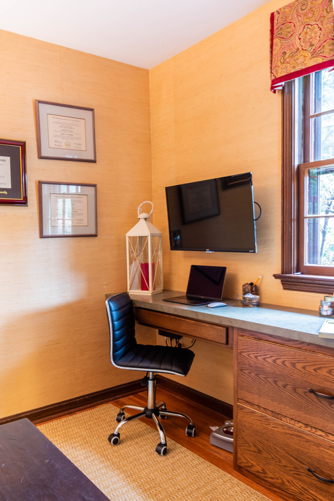Bild på ett litet vintage arbetsrum, med ett bibliotek, mellanmörkt trägolv, ett inbyggt skrivbord, brunt golv och orange väggar