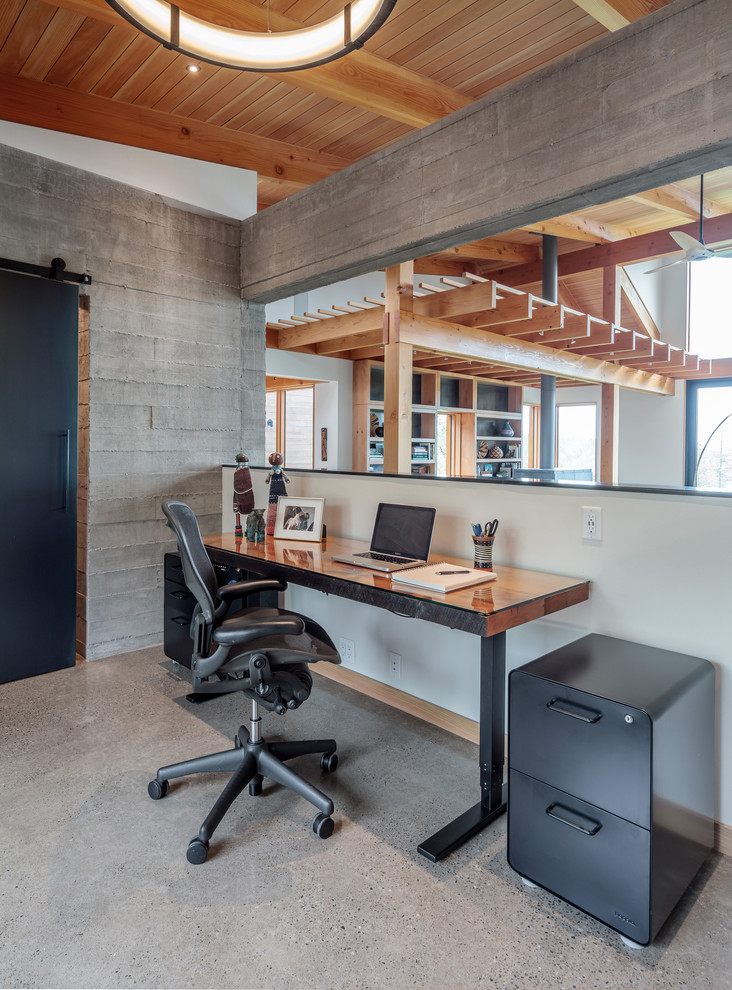 Uriges Arbeitszimmer mit Arbeitsplatz, grauer Wandfarbe, Betonboden, freistehendem Schreibtisch und grauem Boden in Sonstige