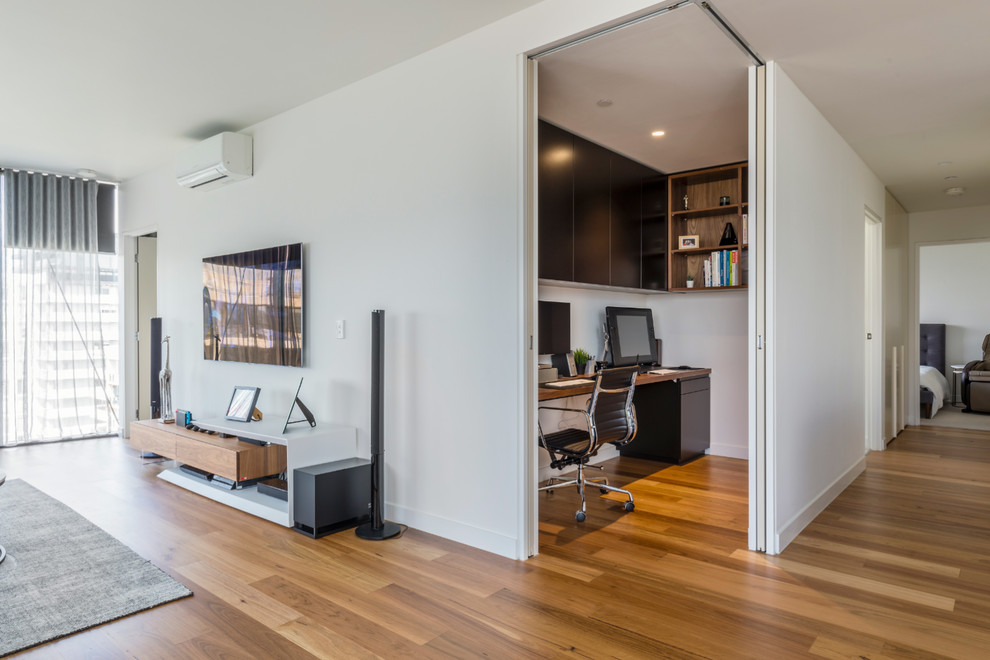 Mittelgroßes Modernes Arbeitszimmer mit Arbeitsplatz, weißer Wandfarbe, braunem Holzboden und Einbau-Schreibtisch in Melbourne