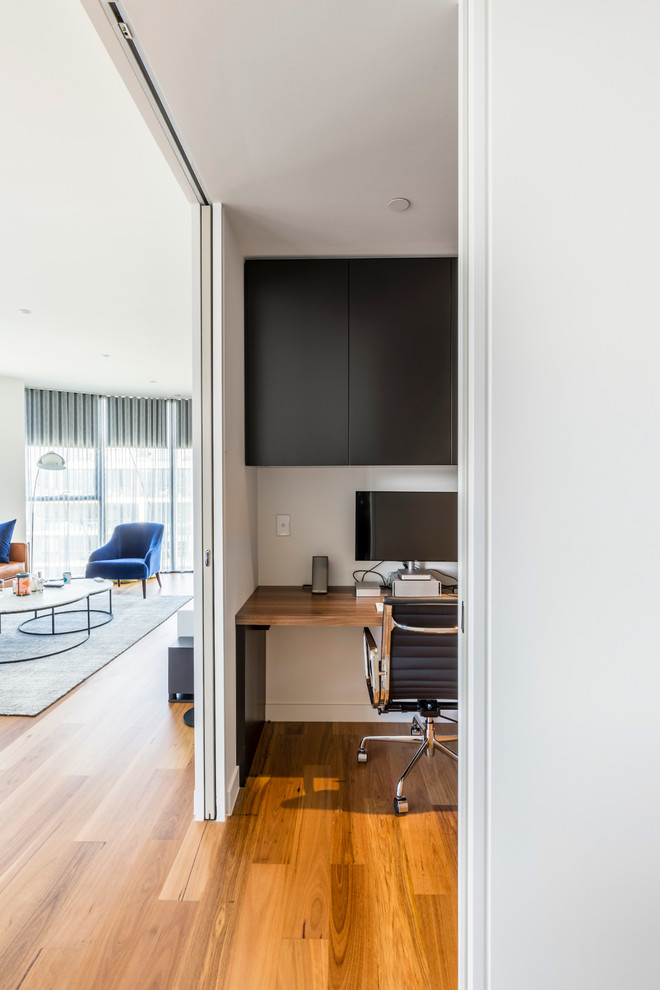 Mittelgroßes Modernes Arbeitszimmer mit Arbeitsplatz, weißer Wandfarbe, braunem Holzboden und Einbau-Schreibtisch in Melbourne
