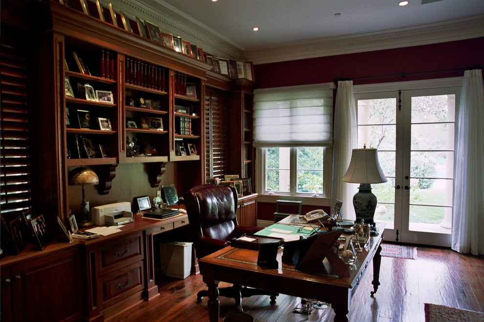 Inspiration för stora klassiska arbetsrum, med röda väggar, mörkt trägolv och ett fristående skrivbord