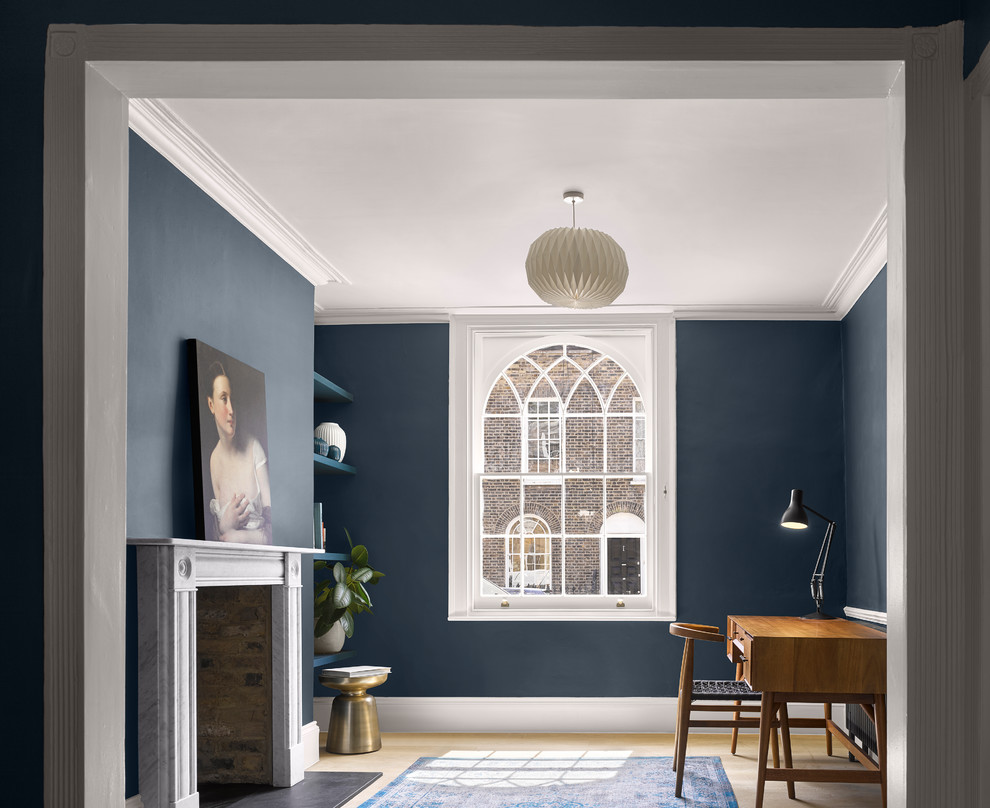 Klassisches Arbeitszimmer mit blauer Wandfarbe, hellem Holzboden, Kamin, Kaminumrandung aus Stein, freistehendem Schreibtisch und beigem Boden in London