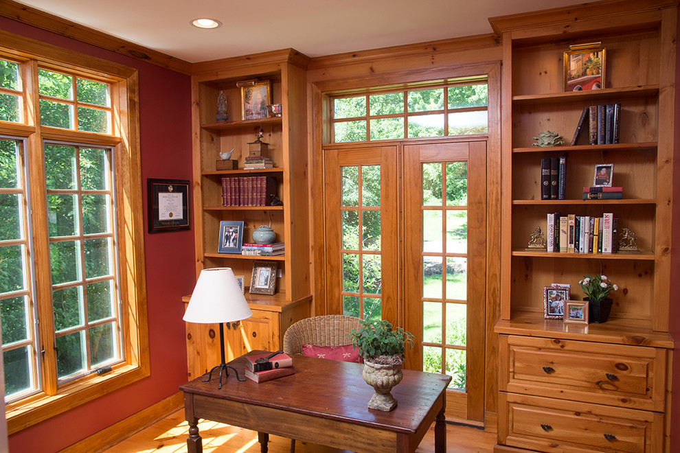 Bild på ett mellanstort rustikt hemmabibliotek, med röda väggar, ljust trägolv och ett fristående skrivbord
