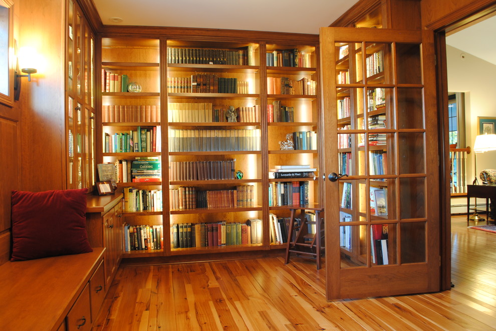 Klassisk inredning av ett mellanstort arbetsrum, med ett bibliotek och mellanmörkt trägolv