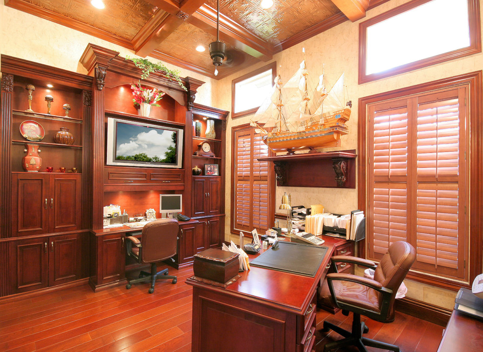 Imagen de despacho clásico grande sin chimenea con paredes beige, suelo de madera oscura, escritorio independiente y suelo rojo