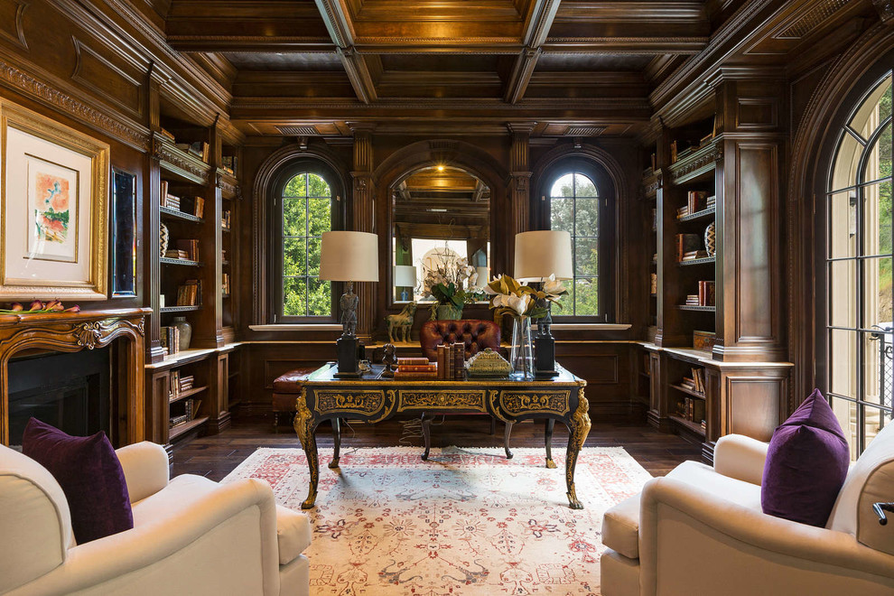 Exempel på ett stort klassiskt hemmabibliotek, med bruna väggar, mörkt trägolv, ett fristående skrivbord, brunt golv, en standard öppen spis och en spiselkrans i trä