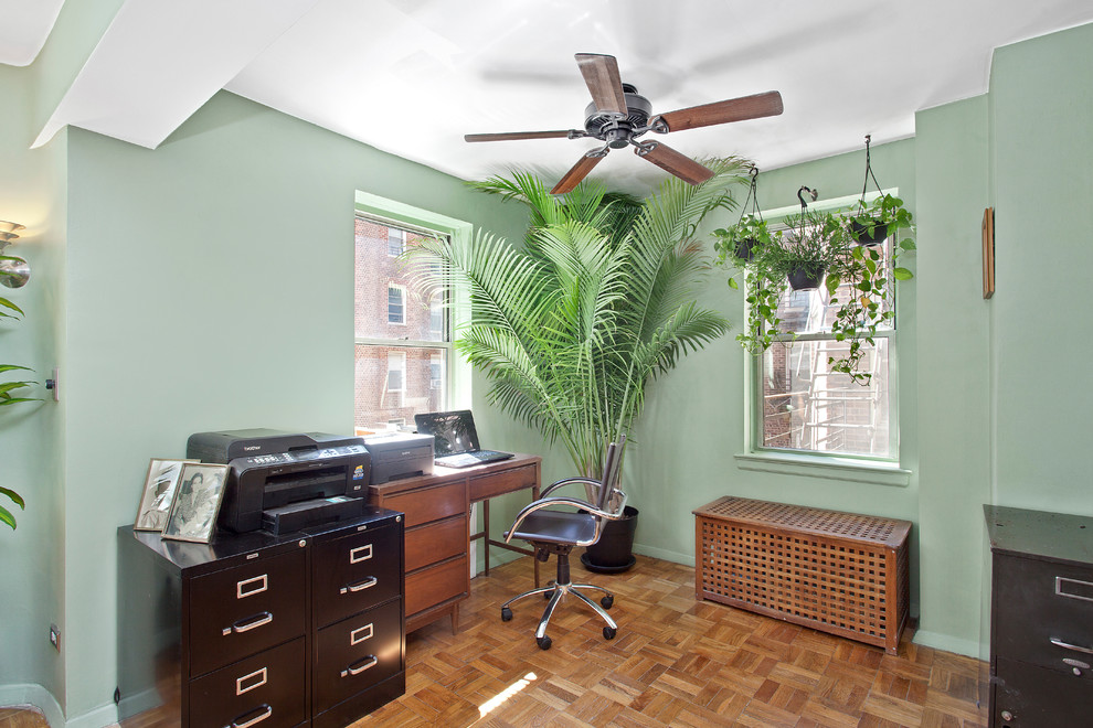 Modelo de despacho tradicional con paredes verdes, suelo de madera en tonos medios y escritorio independiente