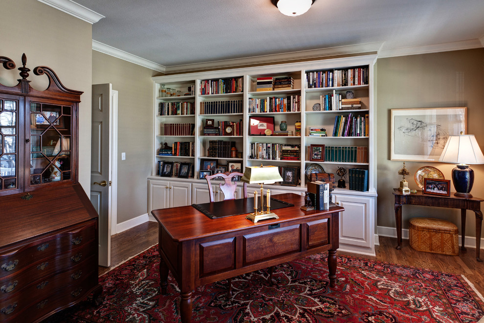 Inredning av ett klassiskt mellanstort hemmabibliotek, med beige väggar, mellanmörkt trägolv och ett fristående skrivbord