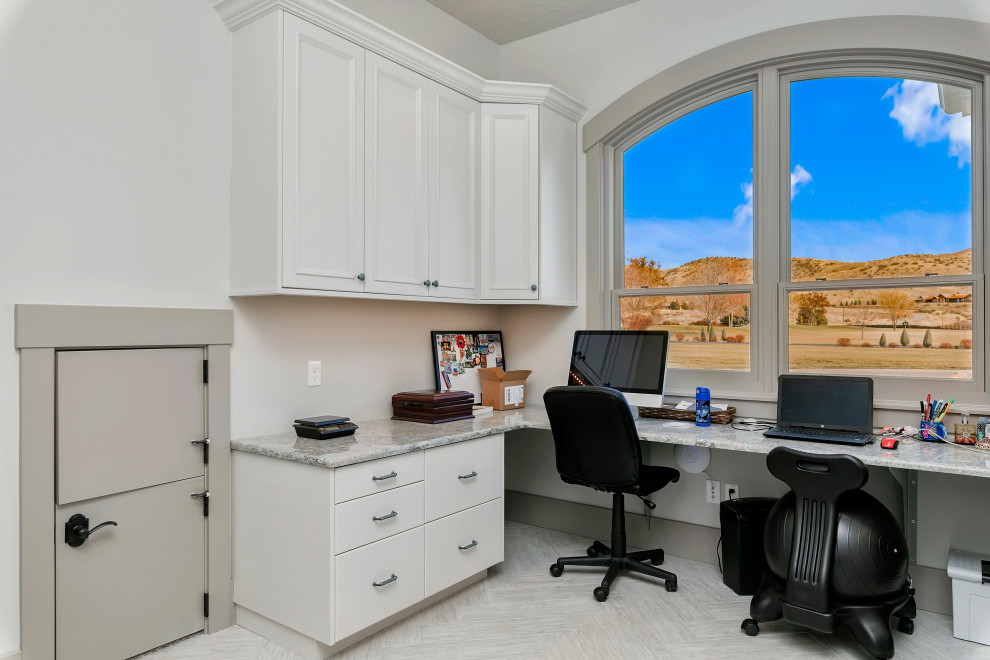 Modelo de despacho tradicional renovado de tamaño medio sin chimenea con paredes blancas, suelo de madera clara, escritorio empotrado y suelo gris