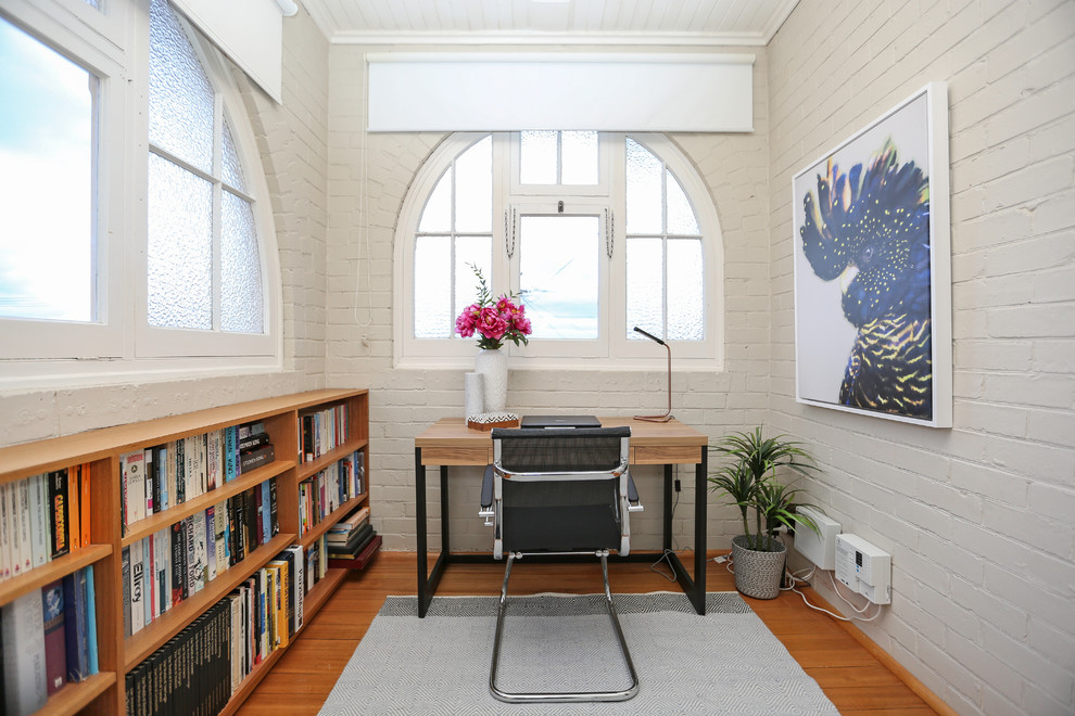 Kleines Klassisches Arbeitszimmer ohne Kamin mit weißer Wandfarbe, braunem Holzboden und freistehendem Schreibtisch in Hobart