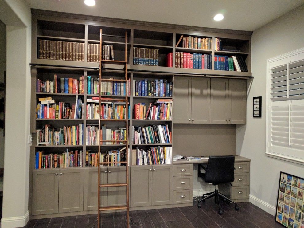 Imagen de despacho clásico renovado de tamaño medio con biblioteca, paredes grises, suelo de madera oscura, escritorio empotrado y suelo marrón