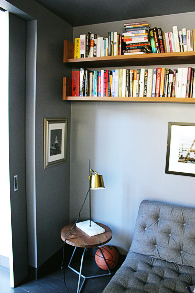 Bild på ett litet funkis arbetsrum, med ett bibliotek, blå väggar, mörkt trägolv, ett inbyggt skrivbord och svart golv