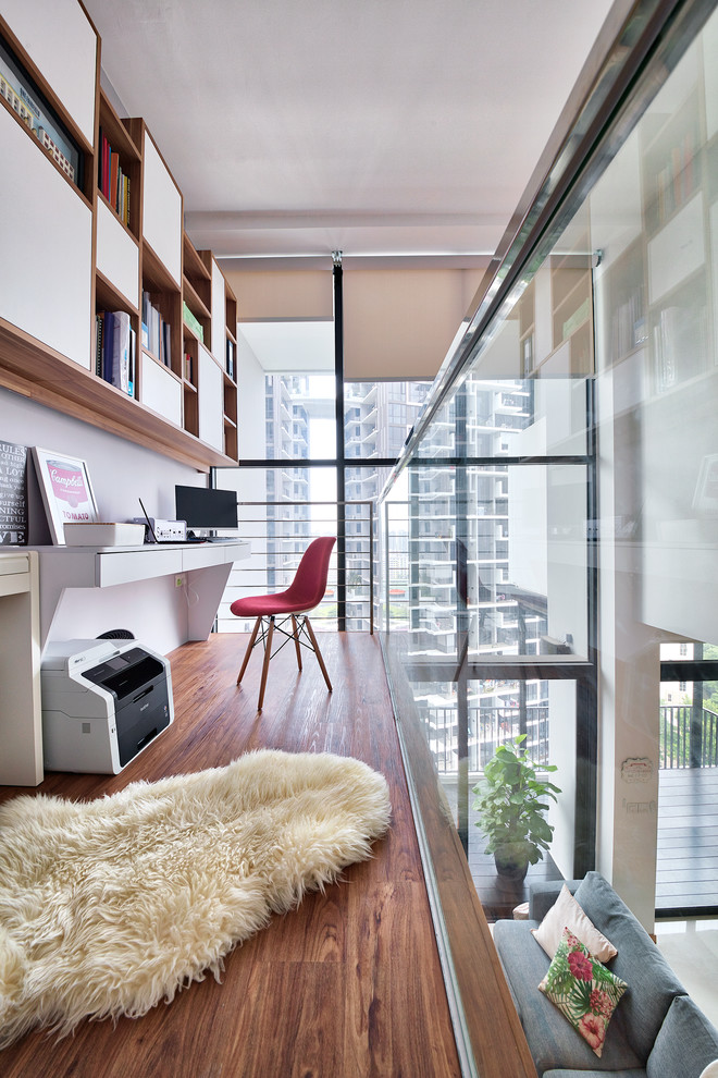 This is an example of a contemporary study in Singapore with white walls, medium hardwood flooring, a built-in desk and brown floors.