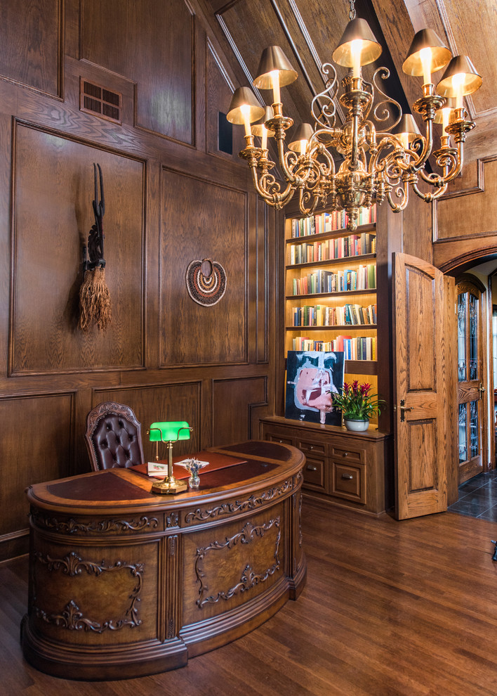 Großes Klassisches Lesezimmer mit brauner Wandfarbe, dunklem Holzboden, Kamin, Kaminumrandung aus Stein und freistehendem Schreibtisch in Los Angeles