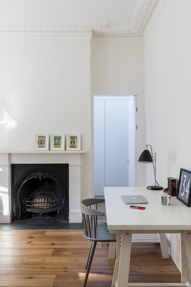 ロンドンにあるお手頃価格の広いモダンスタイルのおしゃれな書斎 (白い壁、無垢フローリング、標準型暖炉、木材の暖炉まわり、自立型机、茶色い床、パネル壁) の写真