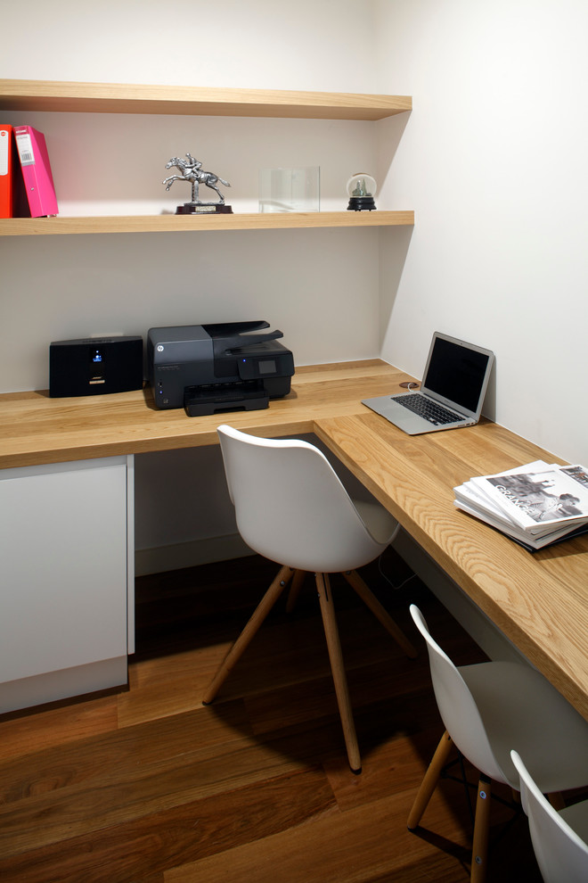 Cette image montre un petit bureau design de type studio avec un mur blanc, un sol en bois brun, aucune cheminée et un bureau intégré.