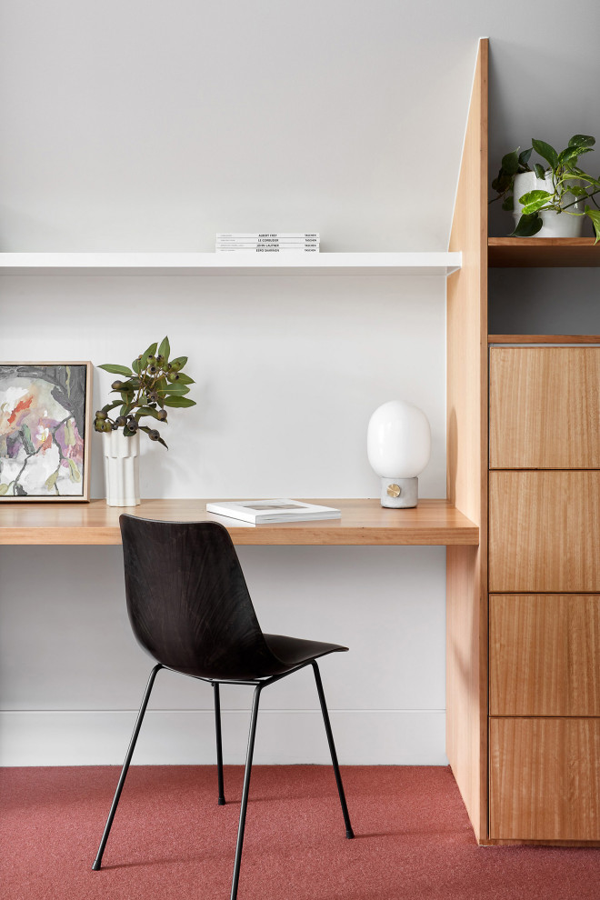 Photo of a large contemporary study in Melbourne with white walls, carpet, a built-in desk and red floors.