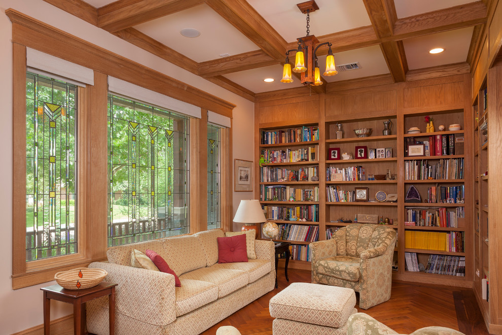 Foto på ett mellanstort amerikanskt hemmabibliotek, med beige väggar och mellanmörkt trägolv