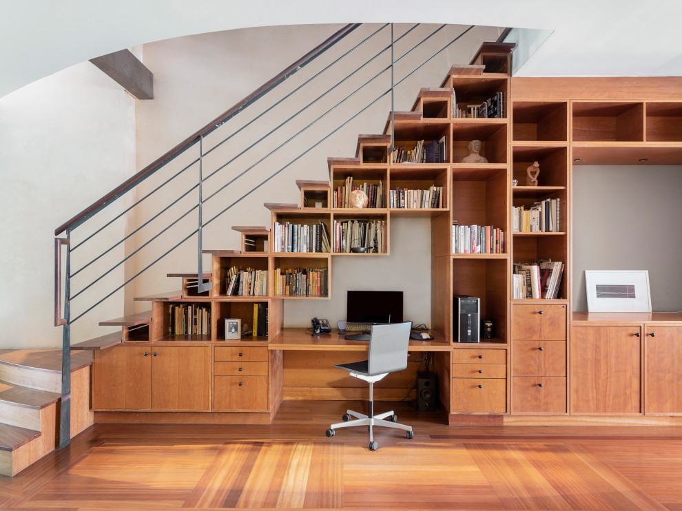 Diseño de despacho contemporáneo pequeño sin chimenea con biblioteca, paredes blancas, suelo de madera en tonos medios y escritorio empotrado
