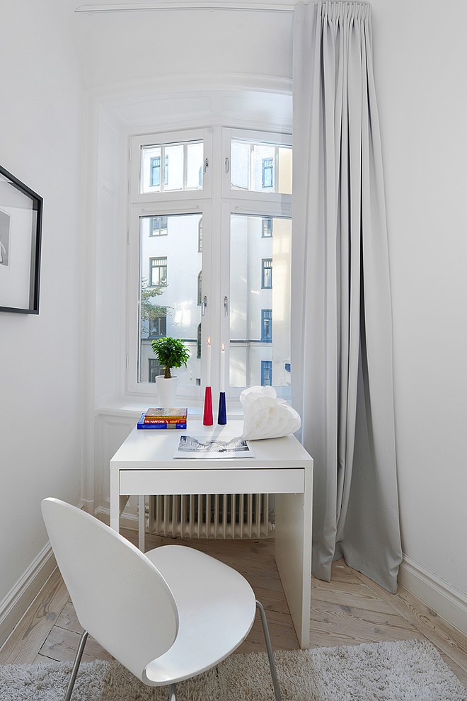 Inspiration för ett litet minimalistiskt hemmabibliotek, med vita väggar, ljust trägolv och ett fristående skrivbord