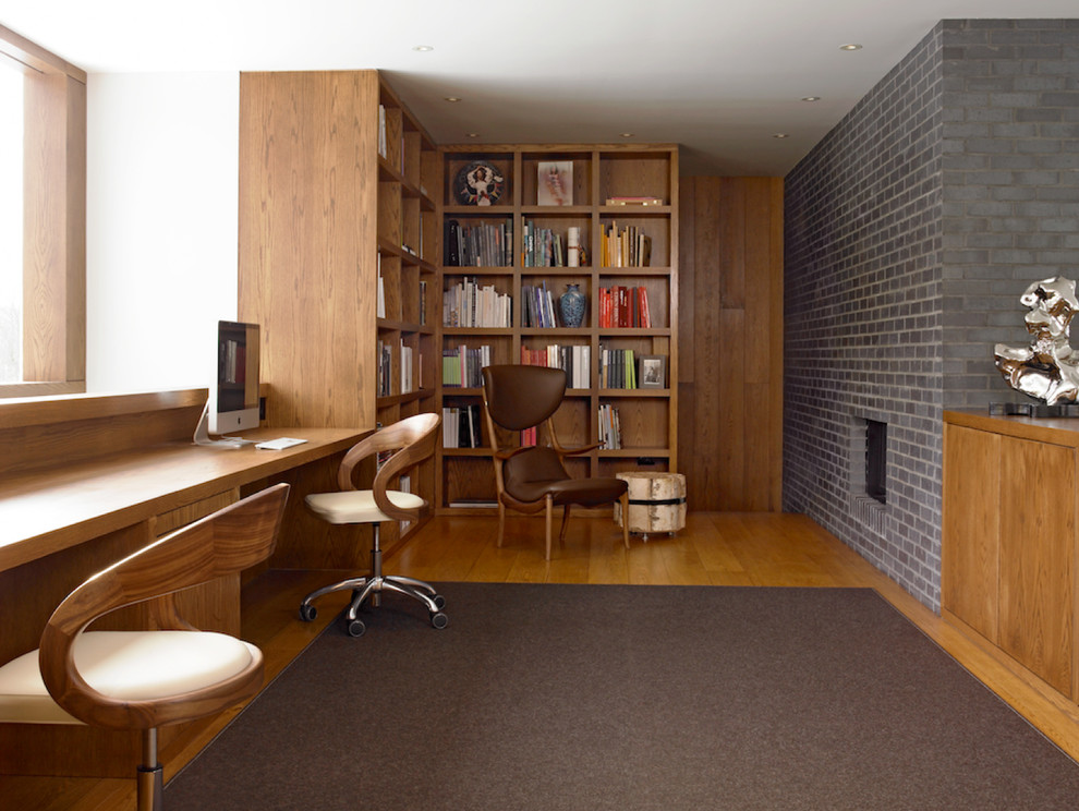 Photo of a medium sized contemporary study in New York with medium hardwood flooring, a built-in desk, white walls, a standard fireplace and a brick fireplace surround.