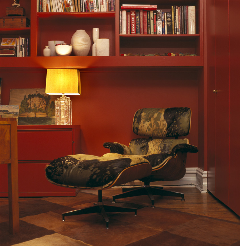 Foto på ett mellanstort funkis hemmabibliotek, med röda väggar, ljust trägolv, en öppen hörnspis, en spiselkrans i tegelsten och ett fristående skrivbord