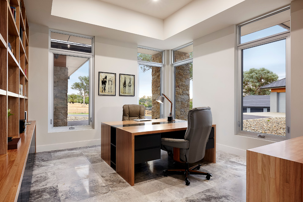 На фото: рабочее место среднего размера в стиле модернизм с серыми стенами, полом из известняка и отдельно стоящим рабочим столом с
