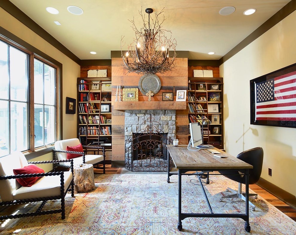 Example of a mid-sized mountain style freestanding desk medium tone wood floor and brown floor home office design in Nashville with a standard fireplace, a stone fireplace and beige walls