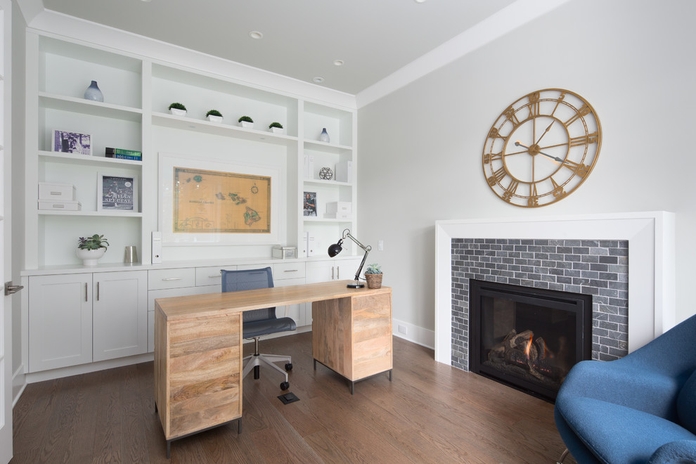 Cette image montre un bureau traditionnel de taille moyenne avec un mur gris, un sol en bois brun, une cheminée standard, un manteau de cheminée en carrelage, un bureau indépendant et un sol marron.