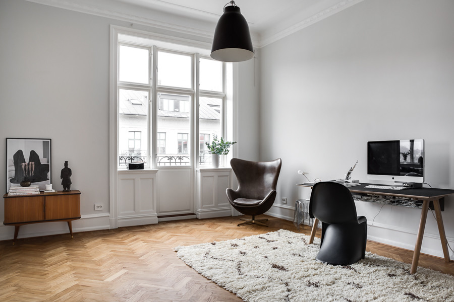Imagen de estudio nórdico grande con paredes grises, suelo de madera en tonos medios y escritorio independiente