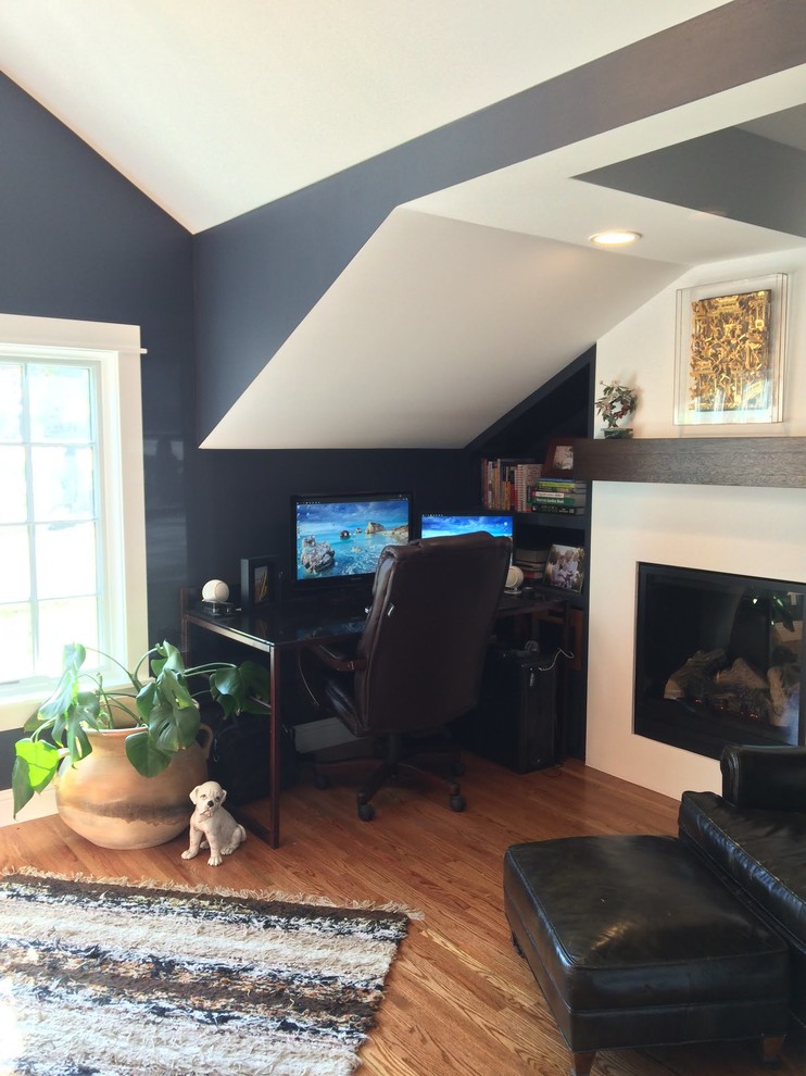 Foto di un ufficio chic di medie dimensioni con pareti nere, pavimento in legno massello medio, camino classico, cornice del camino in intonaco e scrivania autoportante