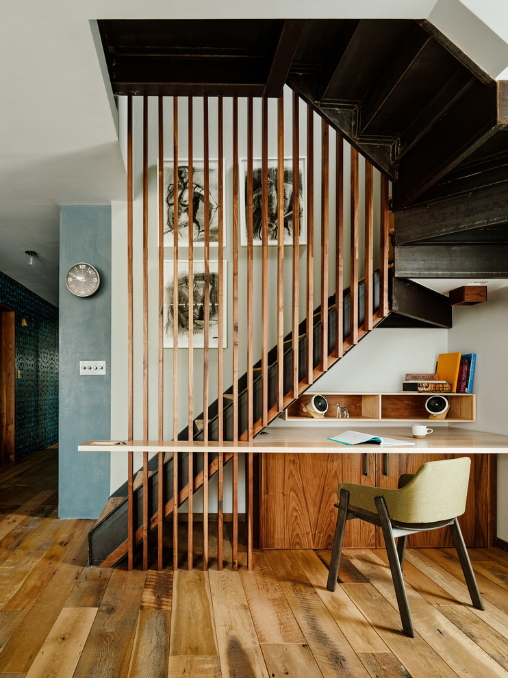 This is an example of a medium sized contemporary home studio in New York with medium hardwood flooring, white walls, no fireplace and a built-in desk.