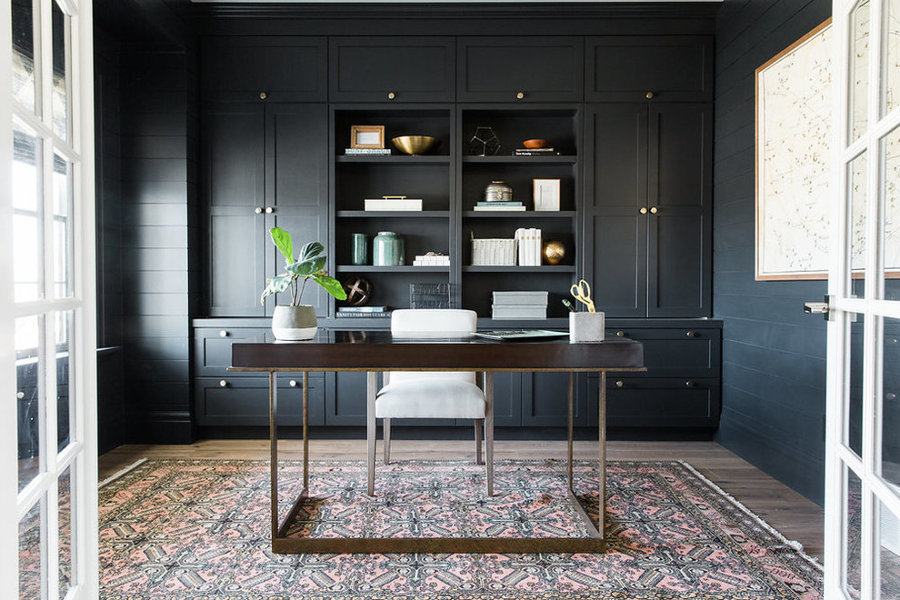 Exempel på ett klassiskt arbetsrum, med mörkt trägolv, ett fristående skrivbord och svarta väggar