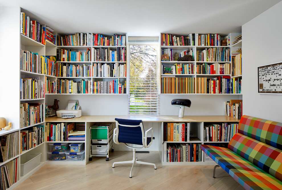 Ejemplo de despacho vintage de tamaño medio sin chimenea con biblioteca, paredes blancas, suelo de madera clara, escritorio empotrado y suelo beige