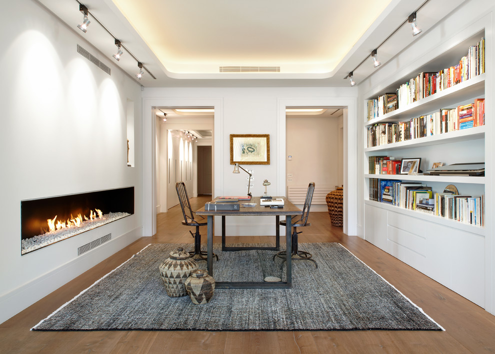 Design ideas for a medium sized urban study in Barcelona with white walls, dark hardwood flooring, a ribbon fireplace, a plastered fireplace surround and a freestanding desk.