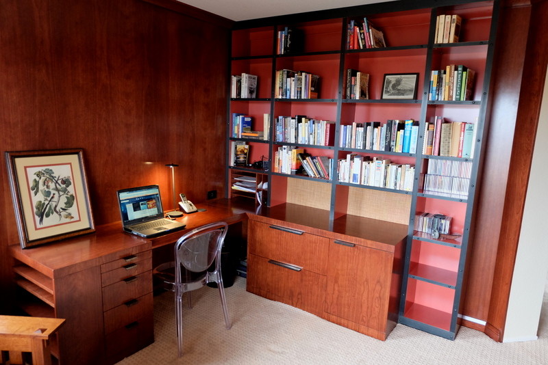 Foto på ett mellanstort eklektiskt hemmabibliotek, med röda väggar, heltäckningsmatta, en spiselkrans i sten och ett inbyggt skrivbord