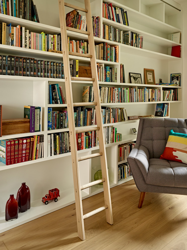 Bild på ett mellanstort hemmabibliotek, med vita väggar, ljust trägolv och ett inbyggt skrivbord