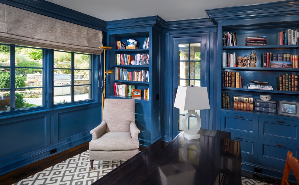 Diseño de despacho tradicional de tamaño medio sin chimenea con biblioteca, paredes azules, suelo de madera oscura, escritorio empotrado y suelo marrón