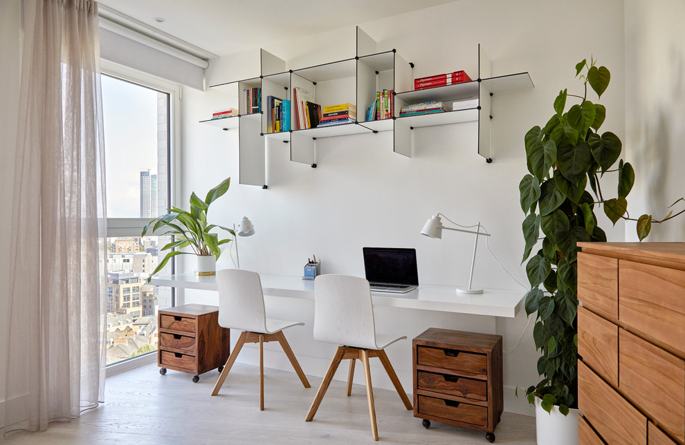 Стильный дизайн: рабочее место в скандинавском стиле с белыми стенами, светлым паркетным полом, встроенным рабочим столом и бежевым полом - последний тренд